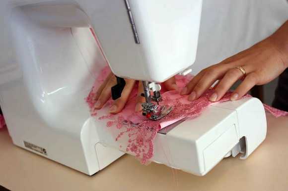 Closeup of a woman's hands sewing pink lace on a sewing machine