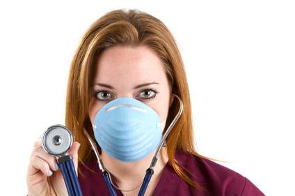 Female nurse wearing scrubs and a surgical mask holds a stethoscope.